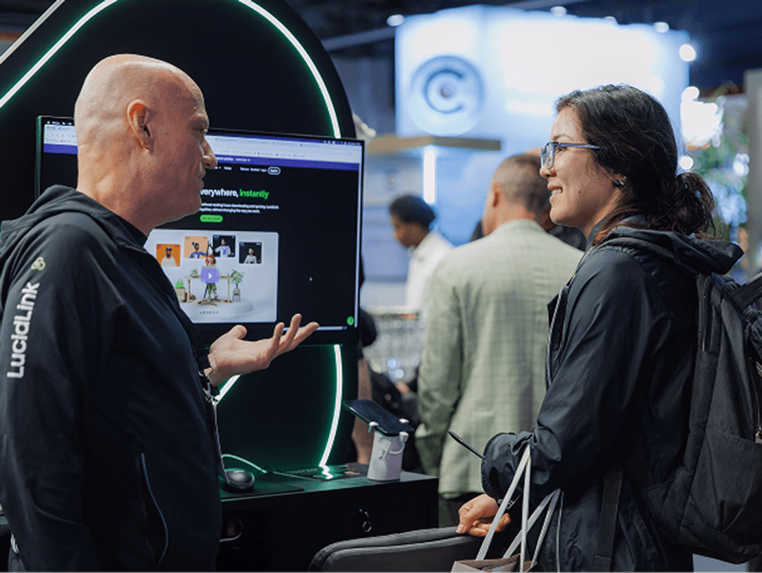 Photo of a man in a LucidLink jacket demonstrating a product on screen to a woman at a trade show booth.