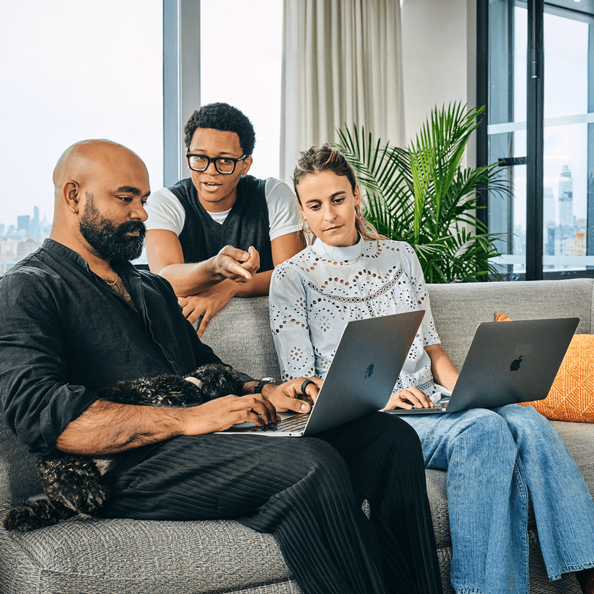 Three colleagues collaborating on laptops on a sofa in a bright, modern office.